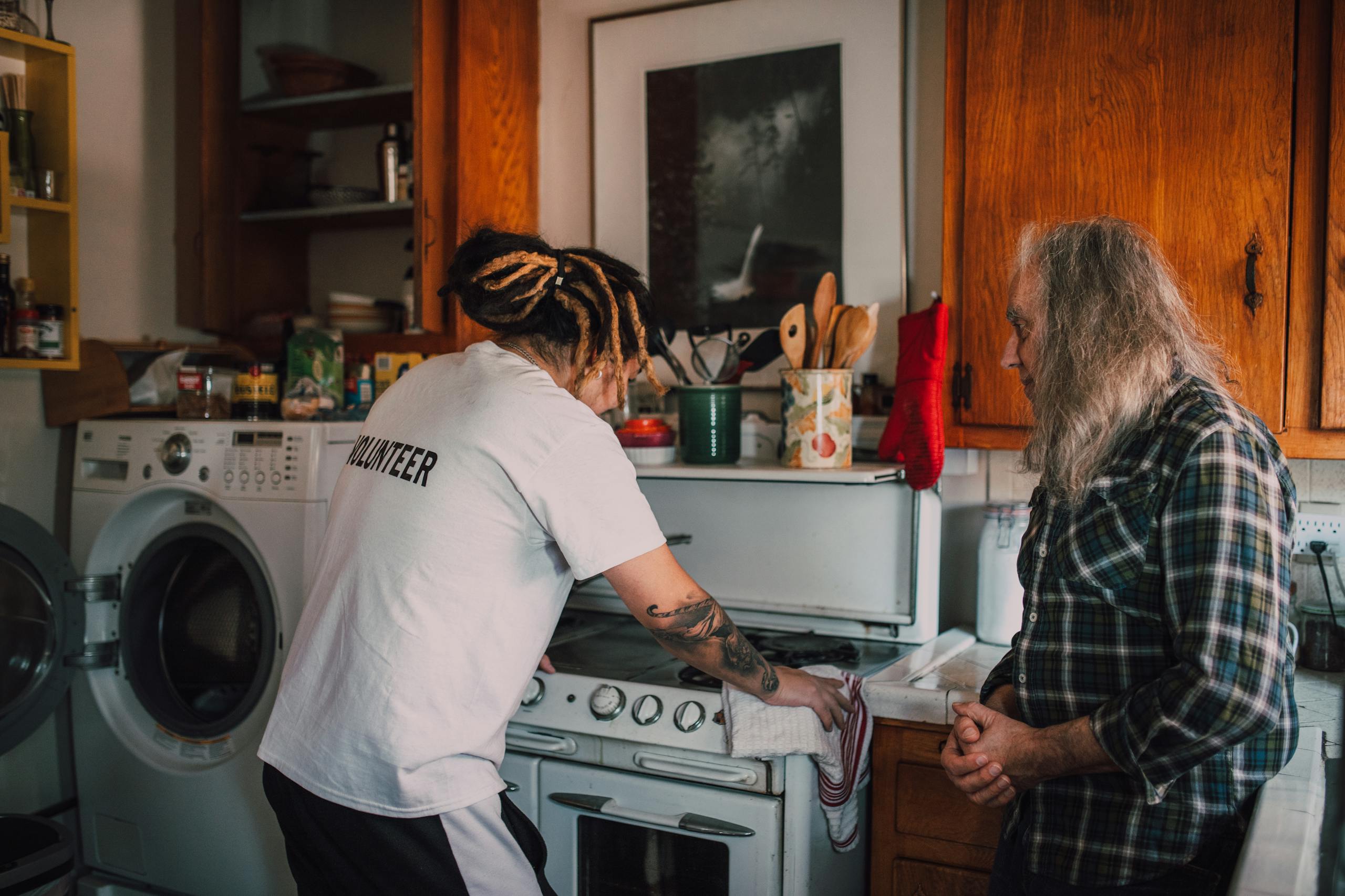 A engineer helps an elderly person in a cozy kitchen, promoting community kindness.
